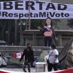 Supporters of presidential candidate Keiko Fujimori carry a large cooking pot as they camp outside the Palace of Justice, hoping to escalate claims of electoral fraud alleged by Fujimori's campaign one month after the presidential runoff election in Lima, Peru, Monday, July 12, 2021. Supporters of both presidential candidates continue to wait for an official winner of the June 6 election. The sign reads in Spanish "Freedom. Respect my vote." (AP Photo/Martin Mejia)
