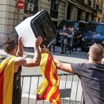 Dos jóvenes muestran una urna empleada el 1-O a los policías nacionales apostados ante la comisaría de la céntrica Via Laietana de Barcelona que permanece cortada por cientos de personas en protesta por la sentencia del procés en la que se condena a los líderes independentistas a penas de entre 9 y 13 años por un delito de sedición. 