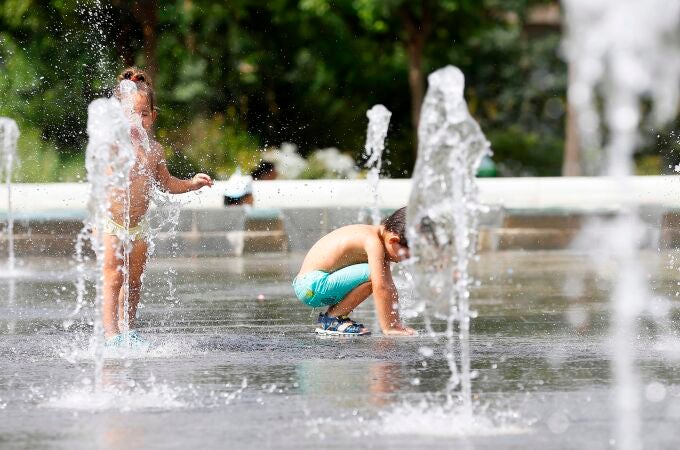 Dos niños juegan en una fuente para mitigar el intenso calor.